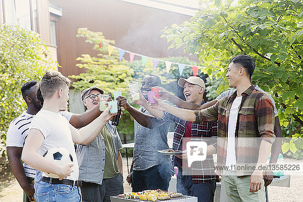 Glückliche männliche Freunde stoßen mit Getränken am Grill im Hinterhof an