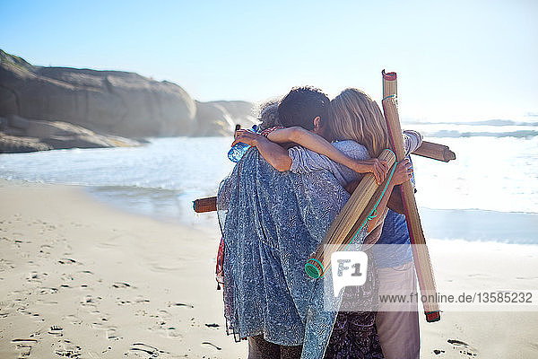 Freundinnen mit Yogamatten umarmen sich am sonnigen Strand während eines Yoga-Retreats