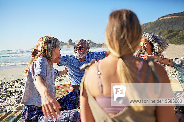 Freunde umarmen sich im Kreis am sonnigen Strand während eines Yoga-Retreats