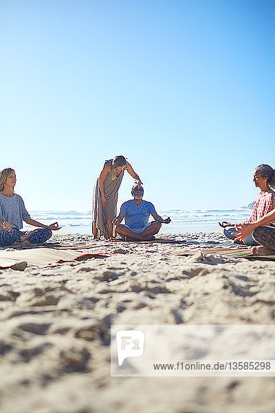 Gelassene Menschen meditieren am sonnigen Strand während eines Yoga-Retreats