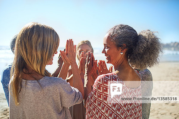 Freundinnen mit verschränkten Händen im Kreis am sonnigen Strand während eines Yoga-Retreats