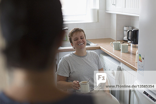 Happy young woman in wheelchair drinking tea in apartment kitchen