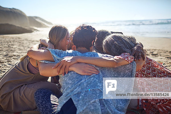 Gruppenumarmung im Kreis am sonnigen Strand während eines Yoga-Retreats