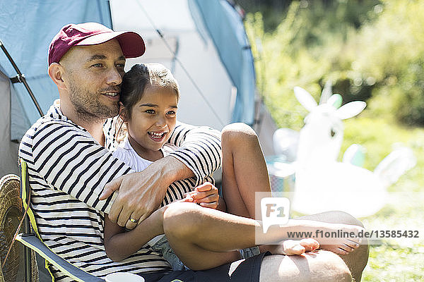 Zärtlicher Vater umarmt Tochter auf sonnigem Campingplatz