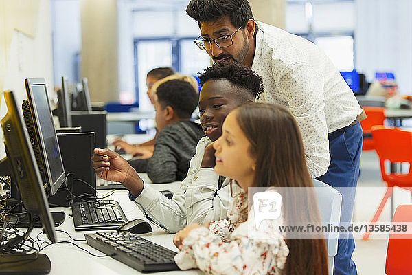 Lehrerin hilft Schülern der Mittelstufe bei der Benutzung eines Computers im Computerraum