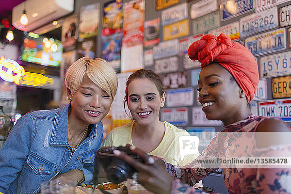 Young women friends using digital camera in bar
