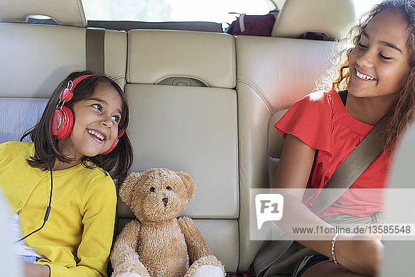 Glückliche Schwestern und Teddybär auf dem Rücksitz eines Autos