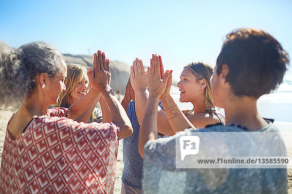 Group standing in circle with hands clasped on sunny beach during yoga retreat