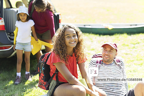 Portrait happy girl camping with family unloading car in sunny field