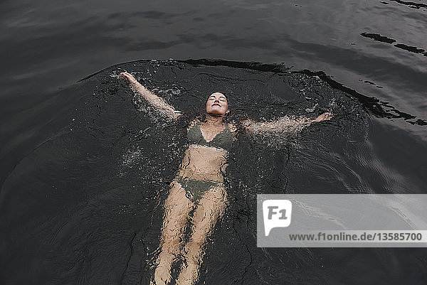 Gelassene junge Frau im Bikini schwimmt im See