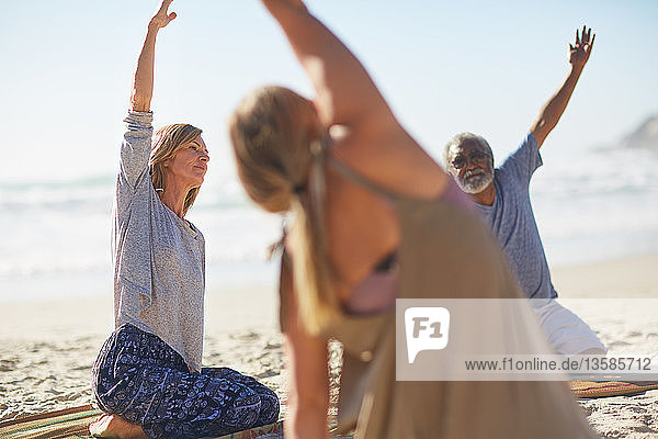 Group stretching on sunny beach during yoga retreat