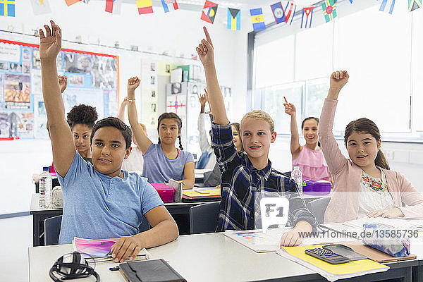 Eifrige Schüler der Junior High School mit erhobenen Händen im Klassenzimmer