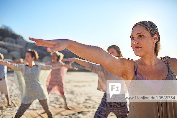Confident woman practicing warrior 2 pose on sunny beach during yoga retreat