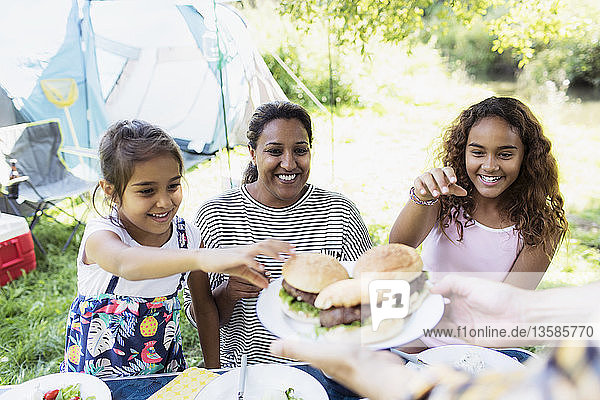 Glückliche Mutter und Töchter greifen auf dem Campingplatz nach gegrillten Hamburgern
