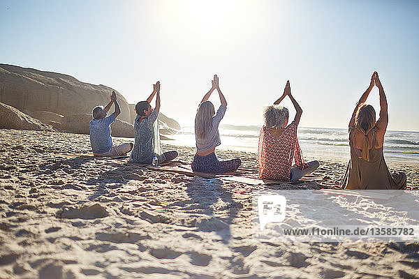 Group practicing yoga on sunny beach during yoga retreat