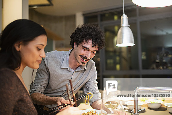 Lächelndes Paar isst Abendessen mit Stäbchen in der Wohnküche