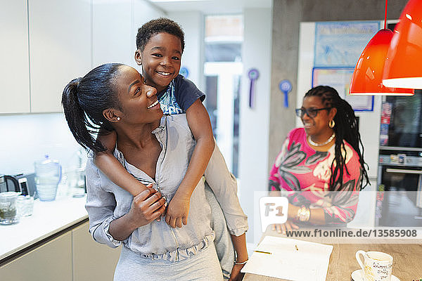 Portrait carefree mother and son piggybacking in kitchen