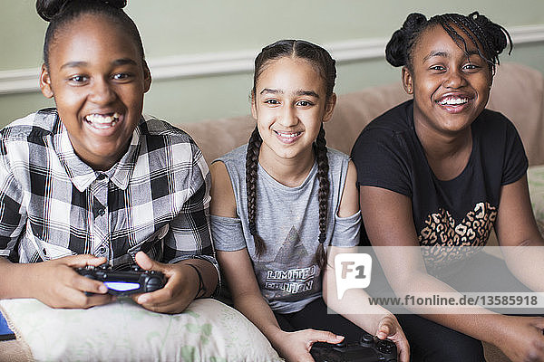 Portrait smiling tween girl friends playing video game on sofa