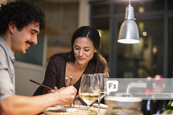 Ehepaar isst mit Stäbchen und trinkt Weißwein in der Wohnküche