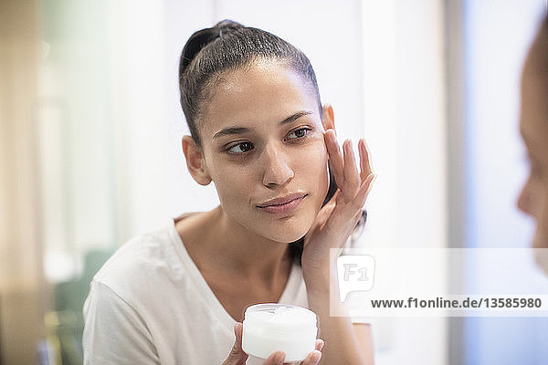 Woman applying moisturizer to face in bathroom mirror
