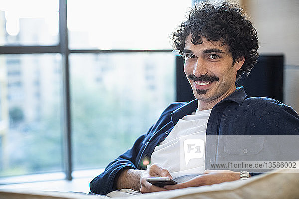 Portrait smiling man using smart phone on sofa