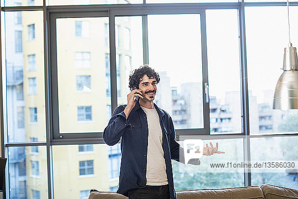 Lächelnder Mann  der in einer städtischen Wohnung mit seinem Smartphone telefoniert