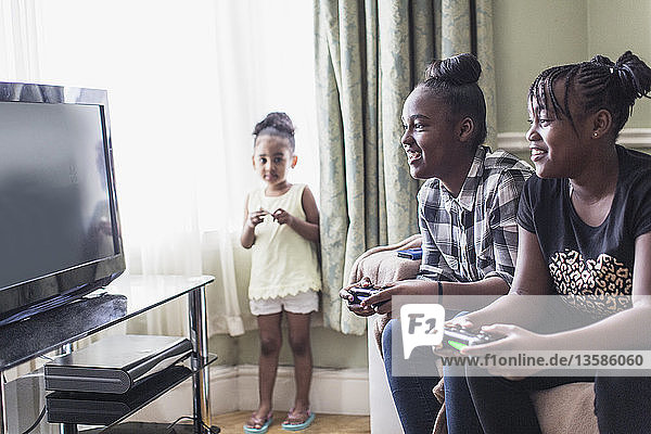 Kleinkind Mädchen beobachten tween Schwestern spielen Videospiel im Wohnzimmer