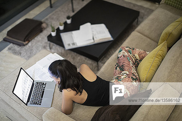 Frau im Schlafanzug arbeitet am Laptop auf dem Wohnzimmersofa