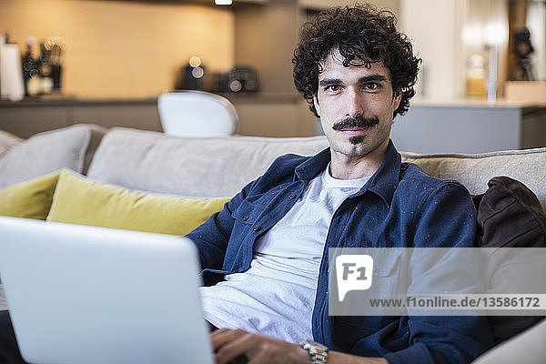 Portrait confident man using laptop on living room sofa