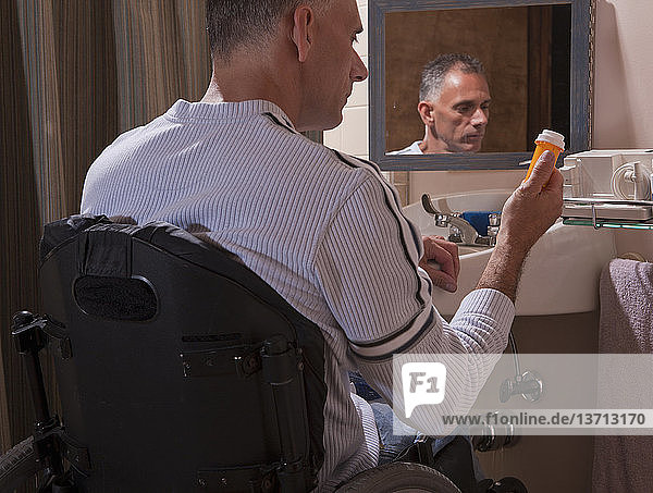 Man with spinal cord injury in a wheelchair looking at a pill bottle