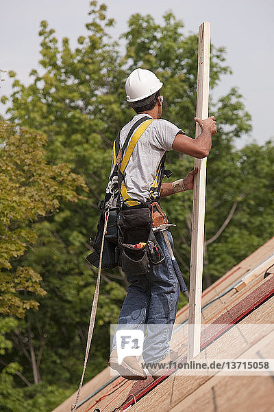 Spanischer Zimmermann trägt Bretter auf dem Dach eines im Bau befindlichen Hauses