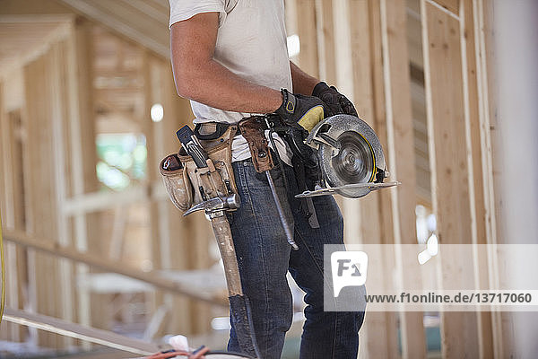 Hispanic carpenter using a circular saw at a house under construction