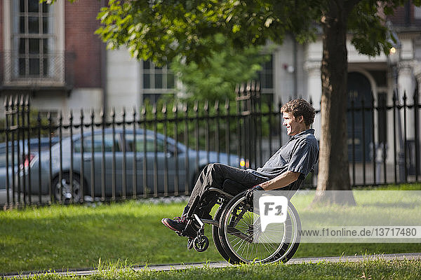Mann mit Querschnittslähmung im Rollstuhl auf einem Weg in einem öffentlichen Park