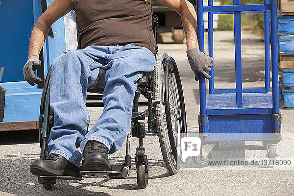 Laderampenarbeiter mit Rückenmarksverletzung im Rollstuhl beim Bewegen einer Sackkarre