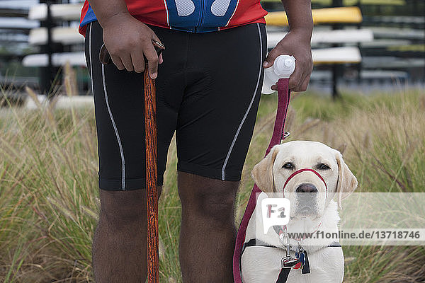 Mann mit Rückenmarksverletzung  der einen Stock benutzt und mit einem Diensthund steht