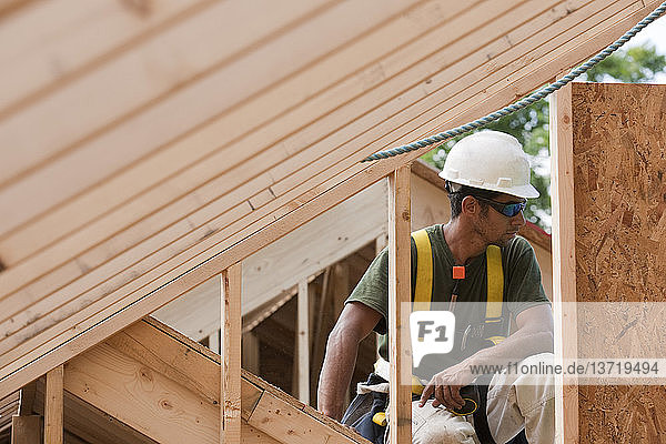 Hispanischer Zimmermann hält ein Maßband im oberen Stockwerk eines im Bau befindlichen Hauses