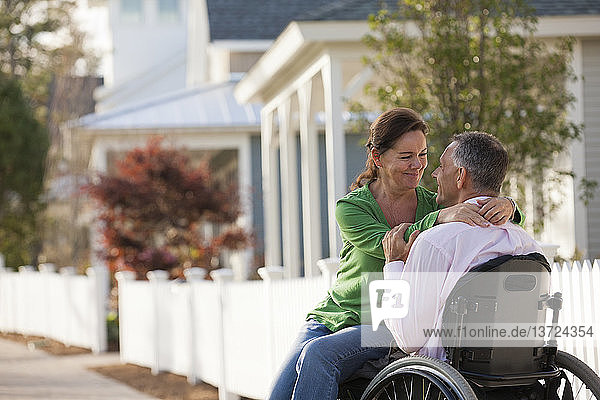 Ein Paar genießt die Gesellschaft des anderen vor seinem Haus  während er im Rollstuhl sitzt