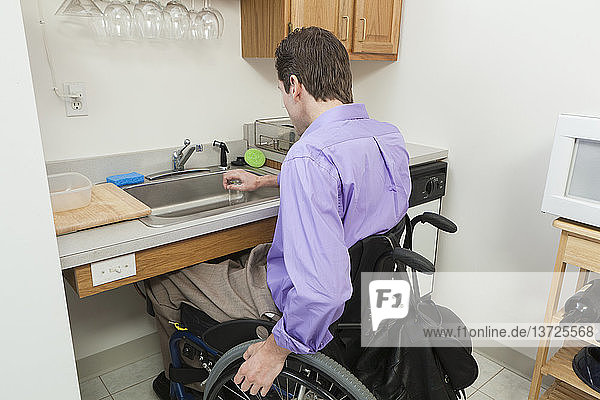 Man in wheelchair with spinal cord injury preparing to wash glass in an accessible kitchen sink