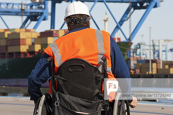 Transportingenieur im Rollstuhl bei der Inspektion von Schiffscontainern und Containerkränen im Verschiffungshafen