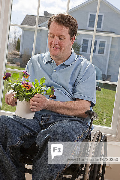 Mann mit Rückenmarksverletzung im Rollstuhl arrangiert Blumen in seiner Wohnung