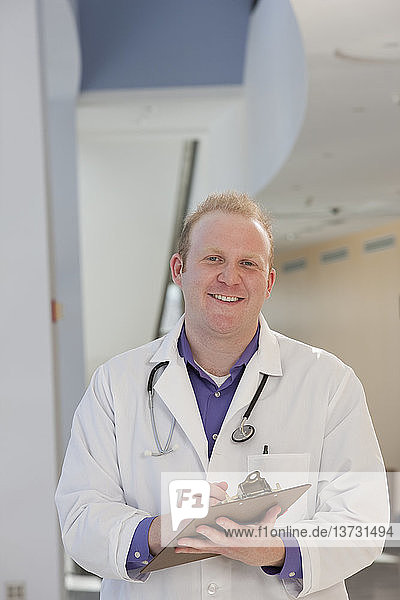 Porträt eines männlichen Arztes  der einen medizinischen Bericht hält und lächelt