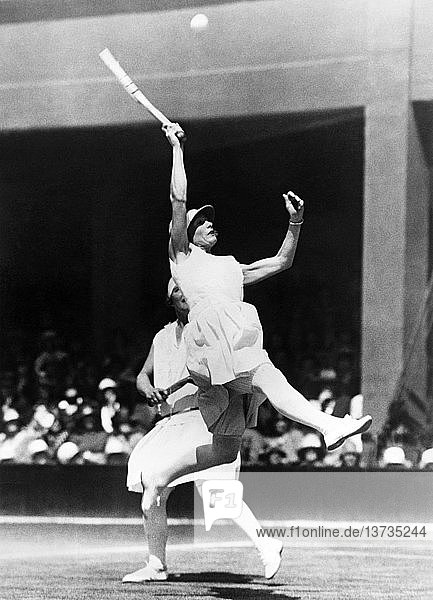 London  England: 1928 Die Niederländerin Kea Bouman versucht im Viertelfinale des Doppelwettbewerbs in Wimbledon mit einem hohen Sprung einen hohen Ball zu erwidern. Ihre Partnerin ist die britische Spielerin Evelyn Colyer.