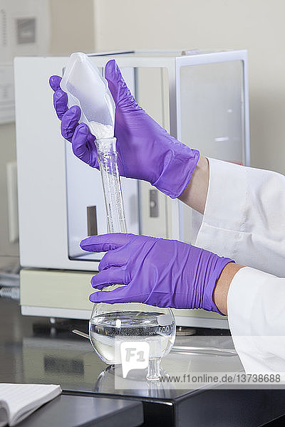 Laborwissenschaftler  der einer Wasserprobe in einem Kolben eine vorher abgemessene Menge eines festen Reagens hinzufügt