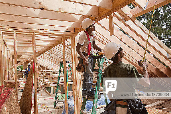 Hispanic carpenters using tape measure at a house under construction