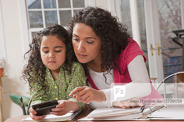 Hispanische Frau  die ihrer Tochter hilft  eine Nachricht auf einem Mobiltelefon zu versenden