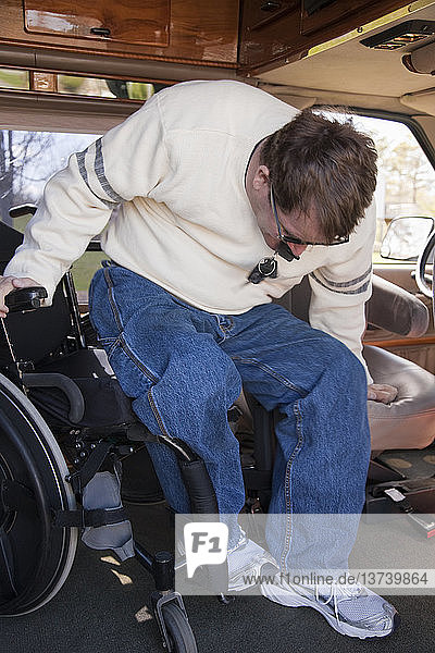 Ein Mann mit einer Rückenmarksverletzung steigt aus seinem Rollstuhl in den Fahrersitz eines behindertengerechten Lieferwagens