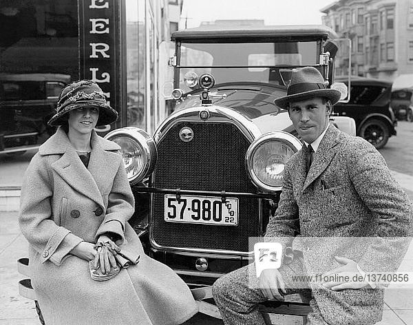 San Francisco  Kalifornien: ca. 1922 Ein Paar vor dem Peerless-Händler  das auf der Stoßstange seines 1922er Peerless mit Colorado-Kennzeichen sitzt.