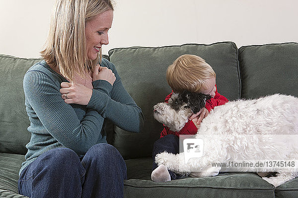Frau gebärdet das Wort ´hug/love´ in amerikanischer Zeichensprache mit ihrem Sohn  der einen Hund umarmt