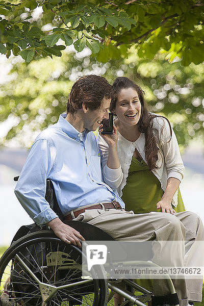 Schwangere Frau hört mit ihrem Mann  der im Rollstuhl sitzt und eine Rückenmarksverletzung hat  auf dem Smartphone