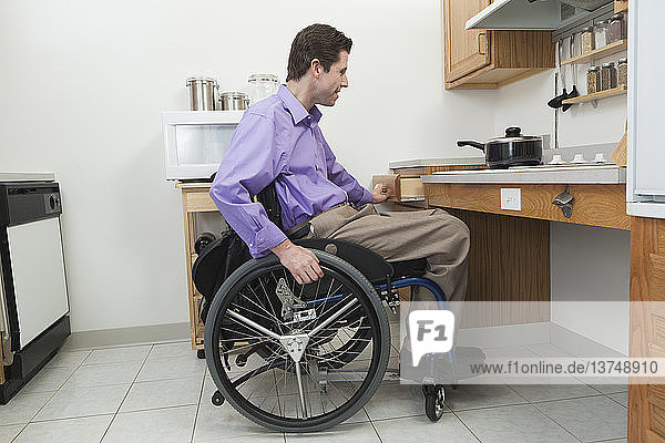 Mann im Rollstuhl mit Rückenmarksverletzung beim Öffnen einer Schublade in einer barrierefreien Küche